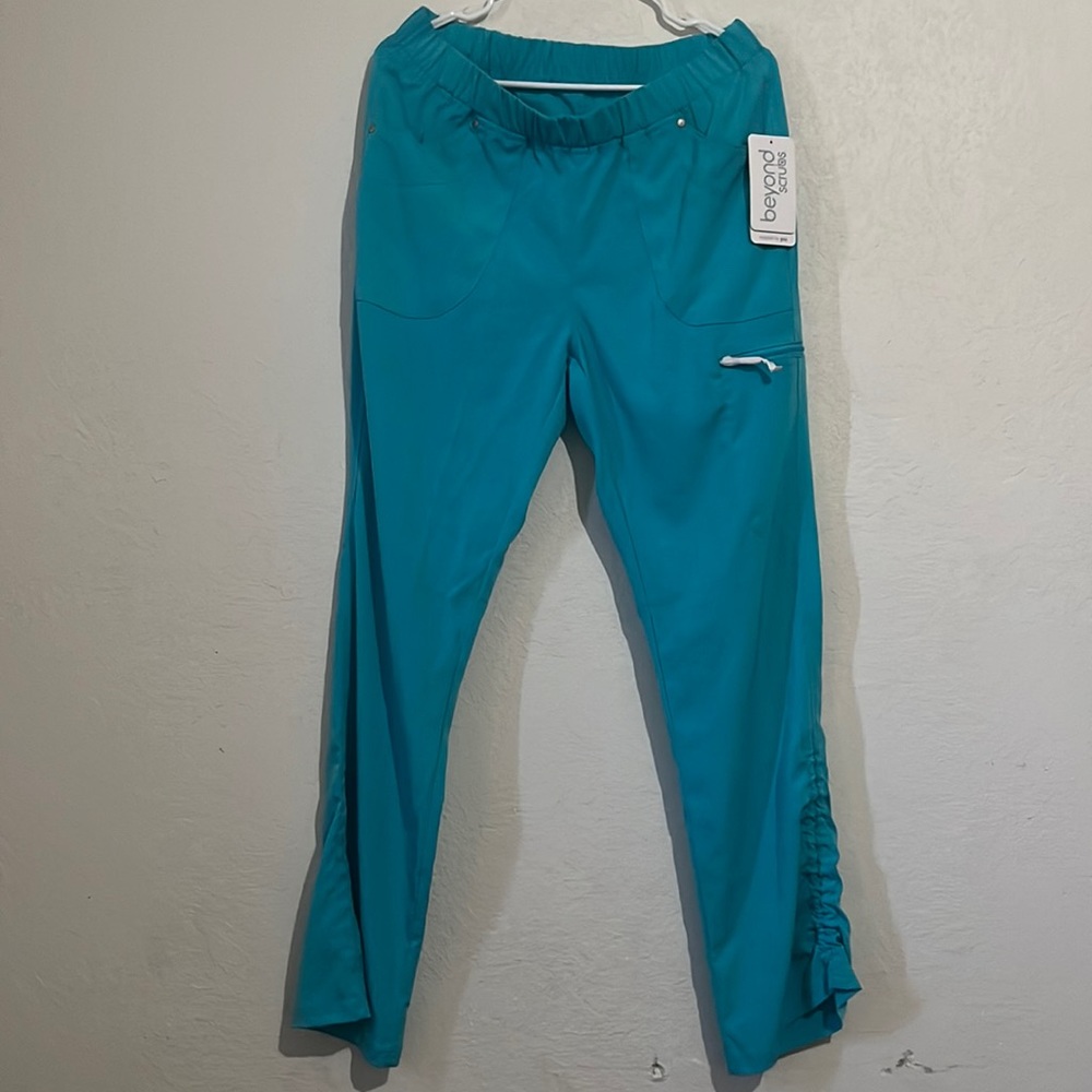 Teal scrubs with five pockets. One is a zip pocket.